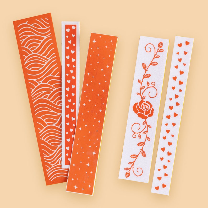 Puede incluir: Cinco rollos de cinta washi con patrones naranja y blanco. Los dise&ntilde;os incluyen corazones, estrellas, una rosa y un patr&oacute;n de ondas.
