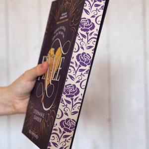 Puede incluir: Un libro de tapa dura de color morado y dorado con el t&iacute;tulo "Fable" en una fuente decorativa. El libro tiene un dise&ntilde;o floral en el lomo.