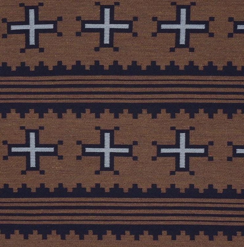 May include: Brown fabric with a repeating pattern of white crosses and dark blue geometric shapes. The design includes horizontal lines and a textured appearance, creating a visually appealing textile.