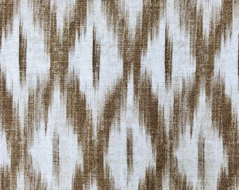 May include: A white fabric with a brown ikat pattern. The fabric has a subtle texture and a slightly blurred effect.