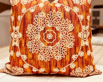 May include: A decorative throw pillow with a brown and orange background and white embroidered floral designs.