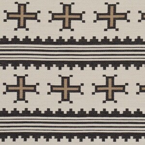 May include: Cream-colored textile with a repeating pattern of brown crosses and black geometric shapes. The design includes horizontal bands of black lines and a textured border, creating a symmetrical and visually appealing pattern.