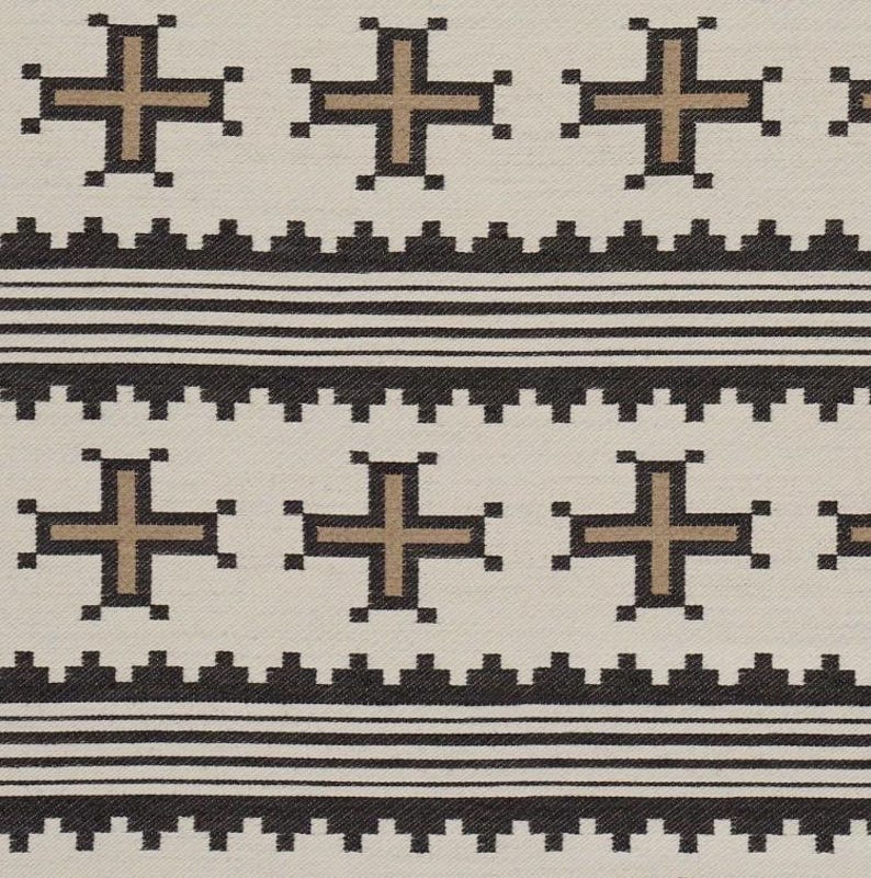 May include: Cream-colored textile with a repeating pattern of brown crosses and black geometric shapes. The design includes horizontal bands of black lines and a textured border, creating a symmetrical and visually appealing pattern.