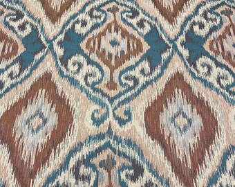 May include: Close-up of a fabric with an ikat design. The pattern features diamond and teardrop shapes in shades of brown, teal, and beige. The fabric has a textured appearance, with a woven or printed effect. The overall design is symmetrical and detailed.