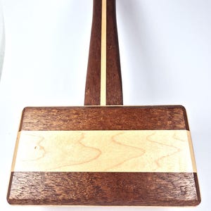 May include: A handcrafted wooden mallet with a rectangular head and a long handle. The head features alternating bands of light and dark wood. The handle has a central light wood stripe and a copper accent at the top. This tool is ideal for woodworking.