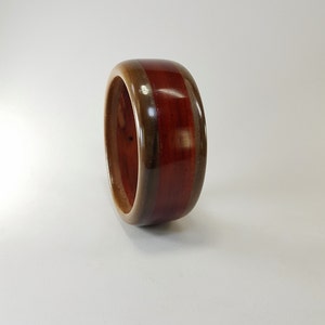 May include: A wooden ring with three layers of wood. The top layer is a dark red wood, the middle layer is a light brown wood, and the bottom layer is a dark brown wood.