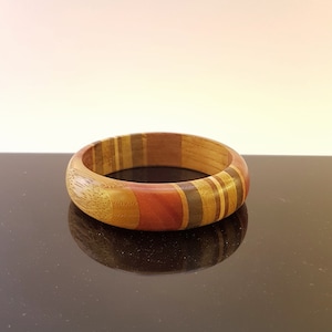 May include: A wooden bangle bracelet with a multi-coloured striped design. The stripes are in shades of brown, red, and yellow.