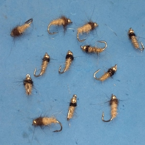 May include: A collection of 11 fly fishing lures with brown and white feathers and black and silver beads.