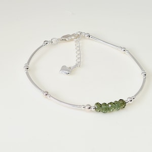 Peut inclure: Un bracelet de cheville argent&eacute; au design d&eacute;licat. Il est compos&eacute; de petites perles rondes et de barres argent&eacute;es incurv&eacute;es. Cinq petites pierres pr&eacute;cieuses vertes &agrave; facettes sont serties au centre. Il poss&egrave;de une cha&icirc;ne r&eacute;glable avec un charm en forme de c&oelig;ur.