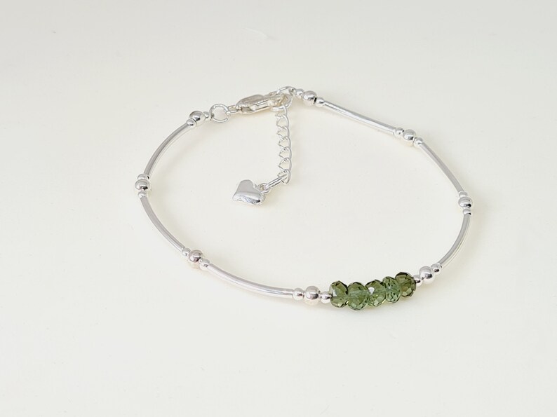 Peut inclure: Un bracelet de cheville argent&eacute; au design d&eacute;licat. Il est compos&eacute; de petites perles rondes et de barres argent&eacute;es incurv&eacute;es. Cinq petites pierres pr&eacute;cieuses vertes &agrave; facettes sont serties au centre. Il poss&egrave;de une cha&icirc;ne r&eacute;glable avec un charm en forme de c&oelig;ur.