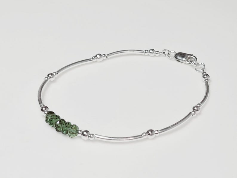 Peut inclure: Un bracelet en argent d&eacute;licat avec de petites perles rondes et cinq pierres pr&eacute;cieuses vertes &agrave; facettes. Le bracelet a un design simple et &eacute;l&eacute;gant avec un fermoir s&eacute;curis&eacute;.