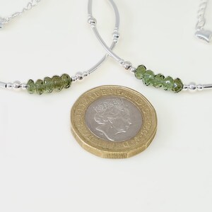 Peut inclure: Deux bracelets en argent avec des perles de pierres pr&eacute;cieuses vertes. Chaque bracelet a un design incurv&eacute; avec de petites perles argent&eacute;es et un charm en forme de c&oelig;ur. Une pi&egrave;ce d'or est au premier plan.