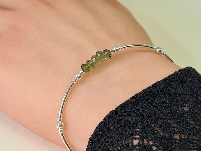 Peut inclure: Un bracelet jonc en argent orn&eacute; d'une rang&eacute;e de pierres pr&eacute;cieuses vert olive facett&eacute;es. Le bracelet a un design simple et &eacute;l&eacute;gant avec de petites perles d'argent. Les pierres pr&eacute;cieuses sont le point central.
