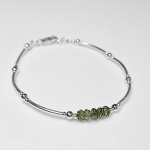 Peut inclure: Un bracelet en argent d&eacute;licat avec de petites perles rondes et cinq pierres pr&eacute;cieuses vert olive facett&eacute;es. Le bracelet mesure environ 18 cm de long et poss&egrave;de une fermeture simple. Le bijou est pr&eacute;sent&eacute; sur fond blanc.
