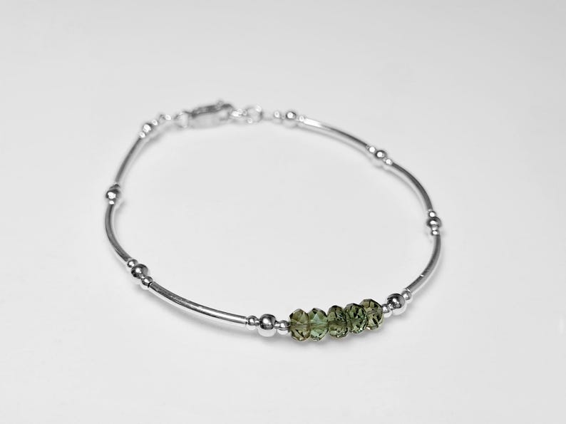 Peut inclure: Un bracelet en argent d&eacute;licat avec de petites perles rondes et cinq pierres pr&eacute;cieuses vert olive facett&eacute;es. Le bracelet mesure environ 18 cm de long et poss&egrave;de une fermeture simple. Le bijou est pr&eacute;sent&eacute; sur fond blanc.