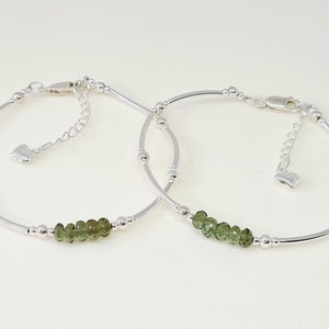 Peut inclure: Deux bracelets argent&eacute;s d&eacute;licats. Chaque bracelet pr&eacute;sente une rang&eacute;e de petites pierres pr&eacute;cieuses vert olive et des perles argent&eacute;es. Les bracelets ont des fermoirs r&eacute;glables et un petit charme en forme de c&oelig;ur.