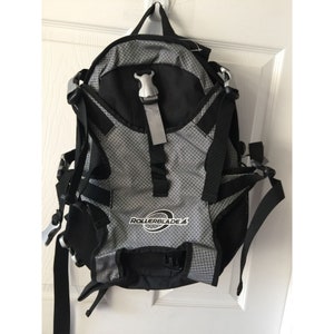 Könnte beinhalten: Ein schwarzer und silberner Rollerblade-Rucksack mit verstellbaren Trägern und einem Netzfach. Der Rucksack hat ein silbernes Logo mit der Aufschrift "Rollerblade".