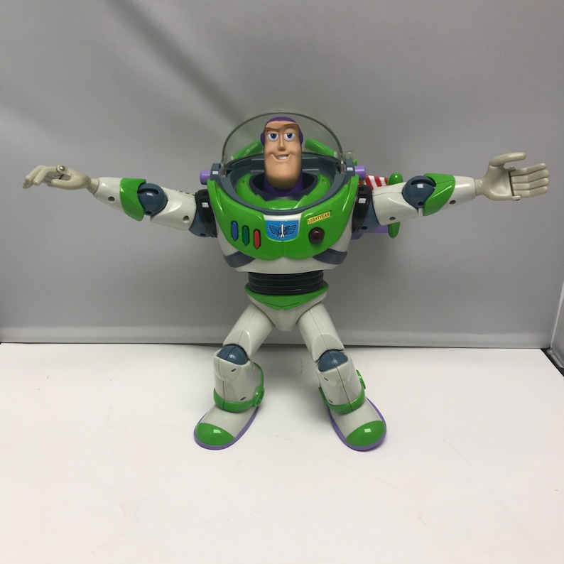 May include: A green and white Buzz Lightyear action figure with a purple helmet and a yellow sticker that says "SPACE RANGER". The figure has articulated arms and legs and is posed with its arms outstretched.