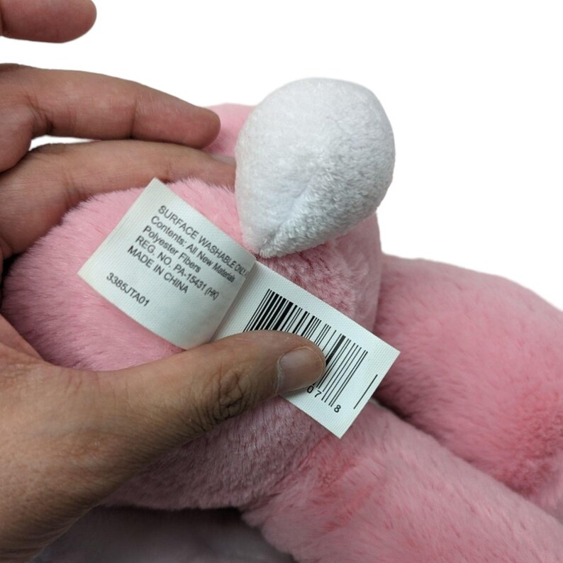 May include: Pink plush toy with a white ear and a tag that reads "SURFACE WASHABLE ONLY", "Contents: All New Material", "Polyester Fibers", "REG. NO. PA-15431 (HK)", "MADE IN CHINA", "3385JTA01".
