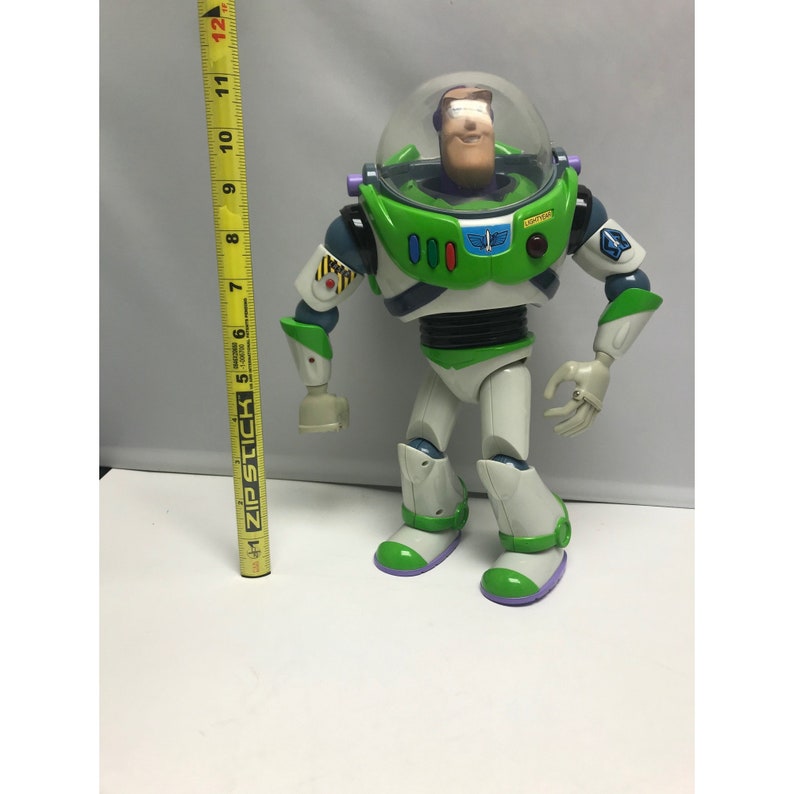 May include: A green and white Buzz Lightyear action figure with a purple helmet and a red button on his chest. The figure is standing on a white surface.
