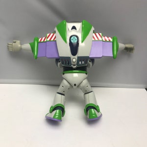May include: A white and green Buzz Lightyear action figure with purple wings and a blue and white face. The figure is in a flying pose with its arms outstretched.