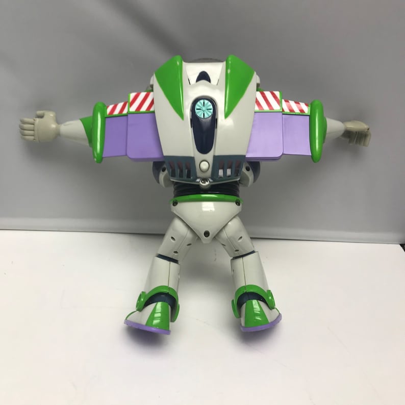 May include: A white and green Buzz Lightyear action figure with purple wings and a blue and white face. The figure is in a flying pose with its arms outstretched.