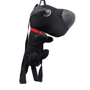 May include: A black plush dog-shaped backpack featuring a large, smooth black nose, a single visible brown and white eye, and a bright red collar. The bag includes adjustable black fabric shoulder straps attached to the back of the plush figure.