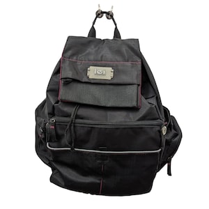 Puede incluir: Mochila negra con ribete rosa y el logo "lei". La mochila tiene múltiples compartimentos con cremallera, un cierre de cordón y un pequeño bolsillo en la parte delantera. La mochila está hecha de un material duradero y resistente al agua.