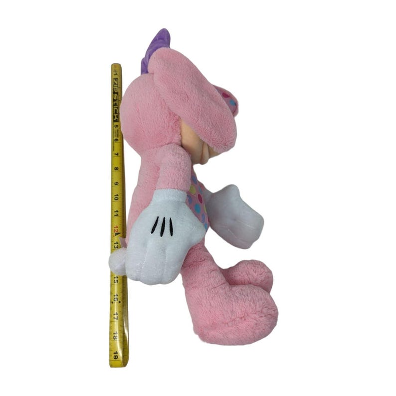 May include: Pink plush toy with a purple bow, white gloves, and colorful polka dots. The toy is sitting on a white background.