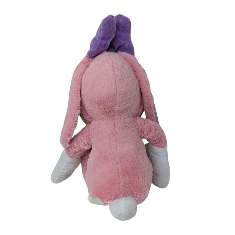 May include: Pink plush bunny rabbit toy with purple ears and a white tail. The bunny is sitting with its arms outstretched.