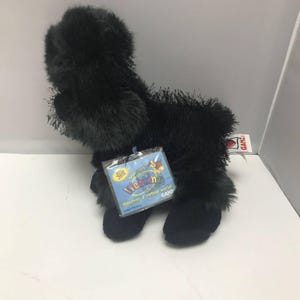 May include: A black plush toy animal with a tag that reads "Webkinz". The toy has a fluffy texture and is standing on four legs. The tag has a blue background with the words "discover a virtual world".