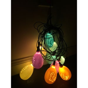 Peut inclure: Une guirlande de lumières en forme d'œuf de Pâques de couleur pastel avec un cordon blanc. Les lumières sont dans différentes nuances de bleu, vert, rose et jaune.