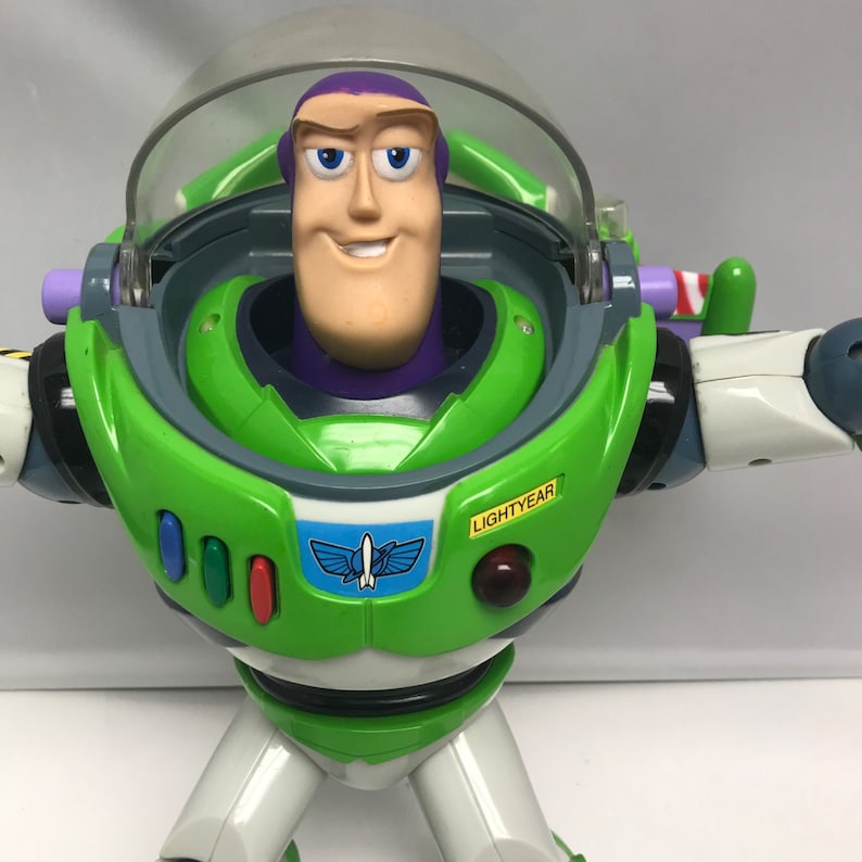 May include: A green and white Buzz Lightyear action figure with a purple helmet and a yellow button that says "LIGHTYEAR".