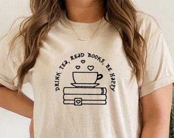 May include: A beige t-shirt with a black graphic design that says "Drink tea, read books, be happy". The graphic includes a cup of tea and a stack of books.
