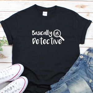 May include: A black t-shirt with white text that reads "Basically a Detective" and a magnifying glass icon.