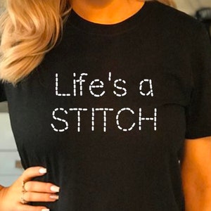 May include: Black t-shirt with white text that reads "Life's a STITCH" in a stitched font.