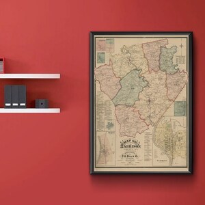 May include: A framed vintage map of Harrison County, with a black frame, hangs on a red wall. The map features detailed county divisions in shades of green, pink, and beige. White shelves hold decorative items.