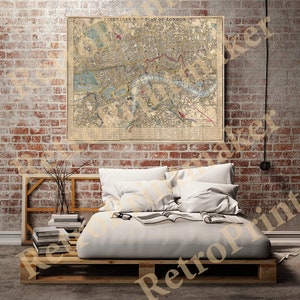 Puede incluir: Un mapa vintage de Londres, titulado "Cruchley's New Plan of London", cuelga de una pared de ladrillo sobre un marco de cama de madera con ropa de cama y almohadas blancas.