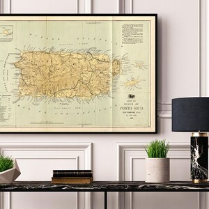 May include: A vintage map of Puerto Rico, framed in black, hangs on a white wall above a black console table. The map shows the island's topography and features the text "Island of Porto Rico".