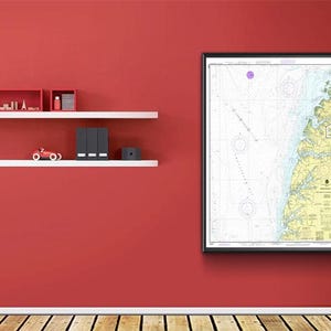 Puede incluir: Un mapa náutico enmarcado con borde negro cuelga de una pared roja. El mapa presenta líneas y colores detallados, que representan áreas costeras. Estantes blancos contienen objetos decorativos, incluyendo edificios en miniatura.