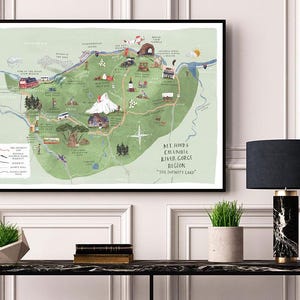May include: A framed print featuring a detailed, illustrated map of the Mt. Hood and Columbia River Gorge region, with landmarks and the text "The Infinity Land." The map is predominantly green with various colourful illustrations.