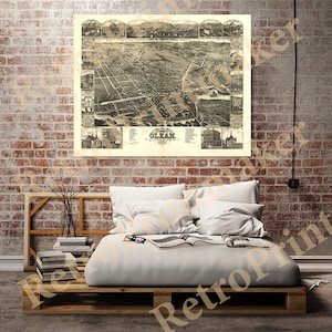 May include: A vintage black and white map of Olean, New York, from 1875. The map shows the city's streets, buildings, and landmarks. The map is framed and hanging on a brick wall.