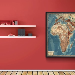 Puede incluir: Un mapa vintage enmarcado de África cuelga de una pared roja. El mapa presenta información geográfica detallada en tonos marrones y azules. Estantes blancos con objetos decorativos están montados en la pared.