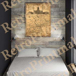 May include: A vintage map of Philadelphia, Pennsylvania, printed on aged paper, hangs on a rustic wood wall above a white bed with two pillows. The map shows the city's layout and surrounding areas, with text and details in a faded brown ink.