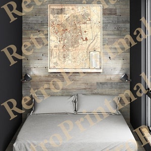 May include: A vintage map of a city is framed and hanging on a wood wall above a bed with white bedding. The map is in black and white with red accents. The wall is made of reclaimed wood planks.