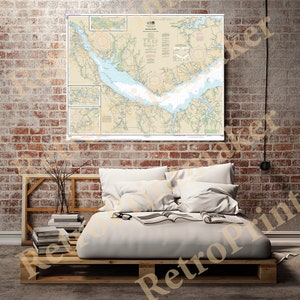 May include: A vintage nautical chart of the Chesapeake Bay, printed on paper with a beige background. The chart shows the waterways, islands, and other features of the bay. The chart is framed and hanging on a brick wall above a bed.