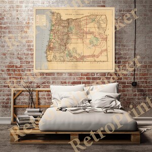 May include: A vintage map of the State of Oregon, printed in brown, red, and green ink on a cream-colored background. The map shows county boundaries, rivers, and railroads. The map is framed and hanging on a brick wall above a bed with white bedding.