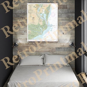 May include: A nautical chart of the Chesapeake Bay, printed on paper and framed in a simple black frame, hangs on a wood-paneled wall above a bed with white linens.