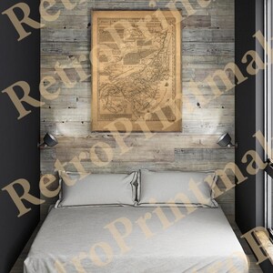 May include: A bedroom with a vintage map print above a bed. The map is framed and mounted on a wooden wall. The bed has a light gray comforter and pillows. Two small lamps are mounted on the wall above the bed.
