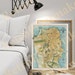 May include: A vintage map of San Francisco, California, framed in a wooden frame. The map is in shades of yellow, green, and blue. The map is titled 'CHEVALIER'S Map of San Francisco' and is dated 1898. The map is displayed on a white wall above a white bed with a white headboard and a black wall lamp.